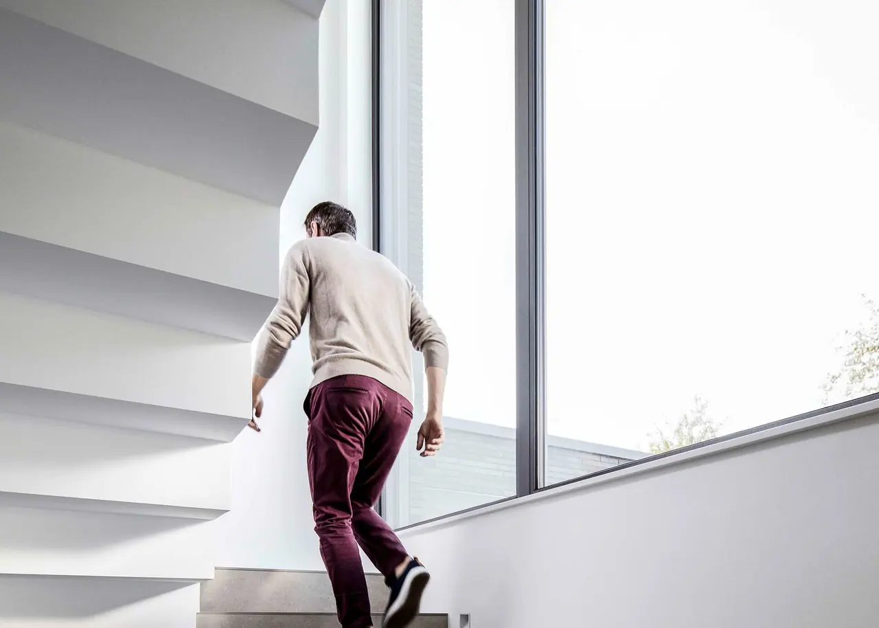 Mann steigt eine Treppe neben einem raumhohen Fenster hinauf